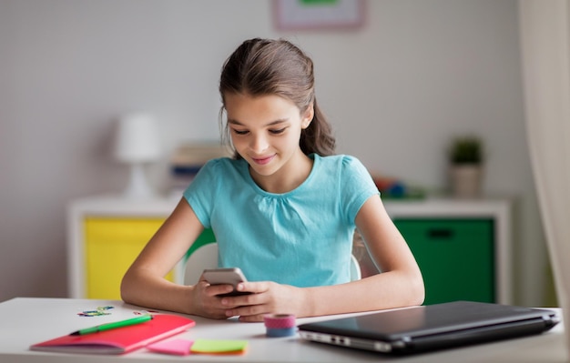 concept d'enfants, de technologie et de communication - fille souriante distrayant des devoirs et textos sur smartphone à la maison