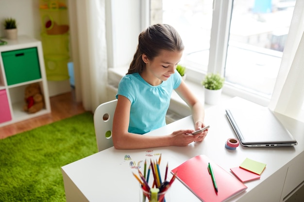concept d'enfants, de technologie et de communication - fille souriante distrayant des devoirs et textos sur smartphone à la maison