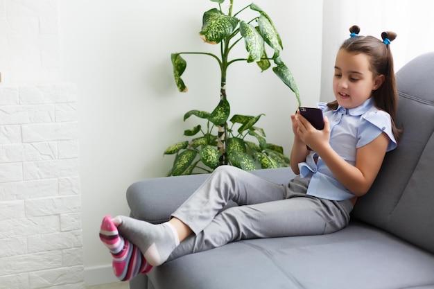 concept d'enfants, de technologie et de communication - fille souriante envoyant des SMS sur un smartphone et allongée dans son lit à la maison