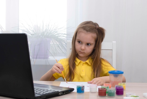 Concept d'enseignement à distance. Une fille apprend à dessiner en ligne pendant l'auto-isolement. Étudiez en ligne. Leçon de dessin avec ordinateur portable. Dessinez une image avec des couleurs. La vie à l'ère numérique. retour à l'école.