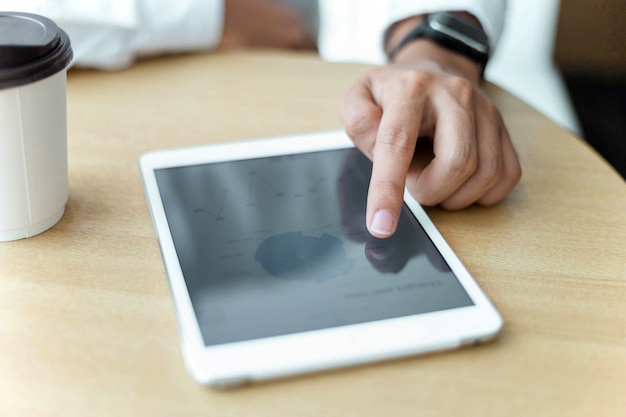 Concept d'entrepreneur une main glissant sur un écran de tablette en plaçant à proximité une tasse de café.