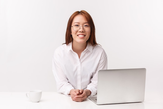 Concept d'entrepreneurs de carrière, de travail et de femmes. Close-up portrait of cheerful young businesswoman sitting in office, maigre table avec ordinateur portable, boire du café, répondre aux questions des clients