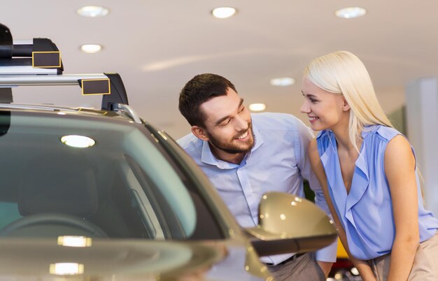 concept d'entreprise automobile, de vente de voitures, de consommation et de personnes - couple heureux achetant une voiture dans un salon de l'auto ou un salon