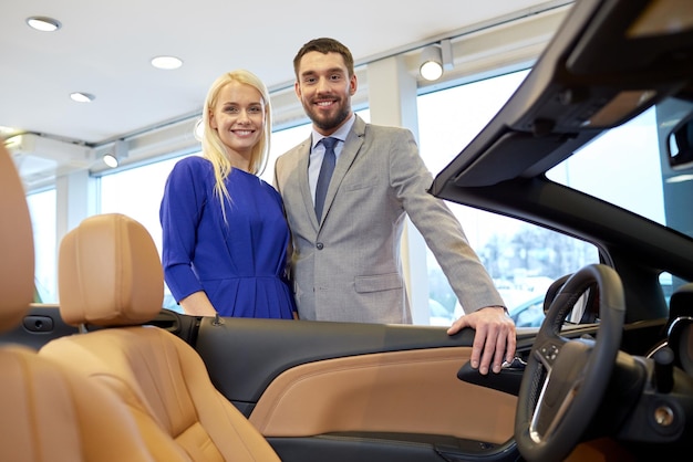 concept d'entreprise automobile, de vente de voitures, de consommation et de personnes - couple heureux achetant une voiture dans un salon de l'auto ou un salon