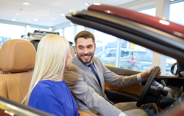 concept d'entreprise automobile, de vente de voitures, de consommation et de personnes - couple heureux achetant une voiture dans un salon de l'auto ou un salon