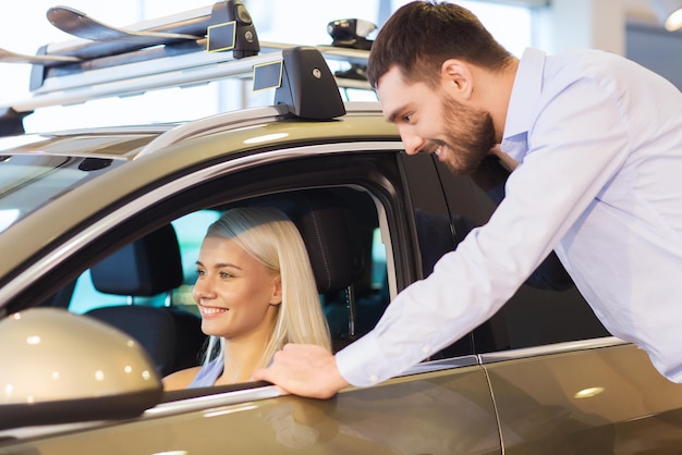 concept d'entreprise automobile, de vente de voitures, de consommation et de personnes - couple heureux achetant une voiture dans un salon de l'auto ou un salon