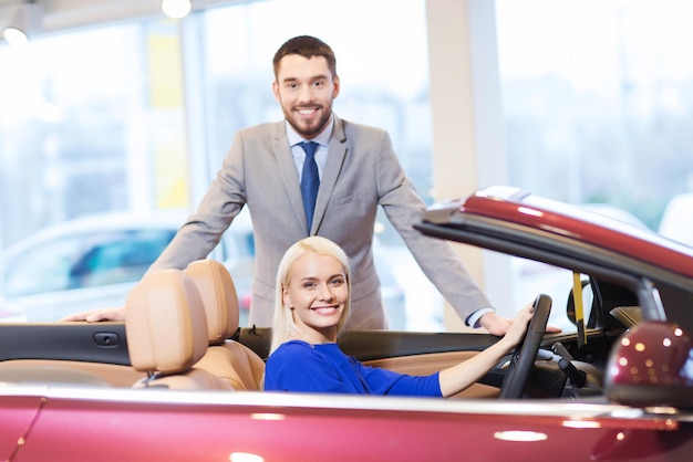 concept d'entreprise automobile, de vente de voitures, de consommation et de personnes - couple heureux achetant une voiture dans un salon de l'auto ou un salon