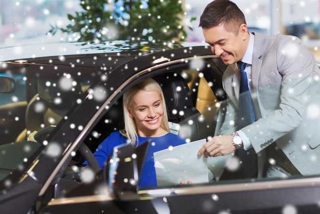 concept d'entreprise automobile, de vente de voitures, de consommation et de personnes - femme heureuse avec un concessionnaire automobile dans un salon de l'auto ou un salon sur l'effet de neige