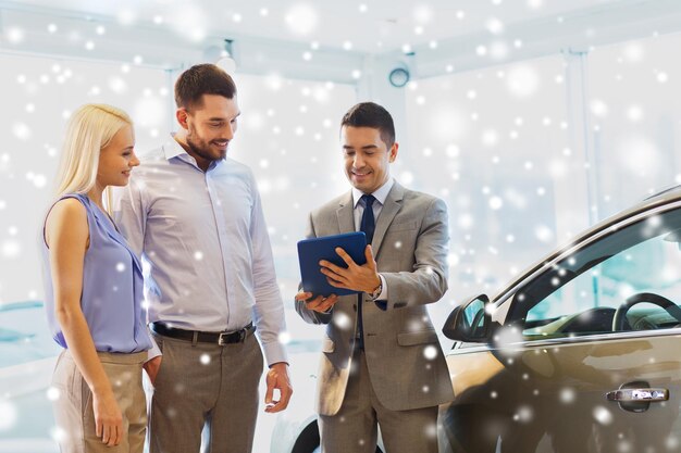 concept d'entreprise automobile, de vente de voitures, de technologie et de personnes - couple heureux avec un concessionnaire automobile dans un salon de l'auto ou un salon sur l'effet de neige