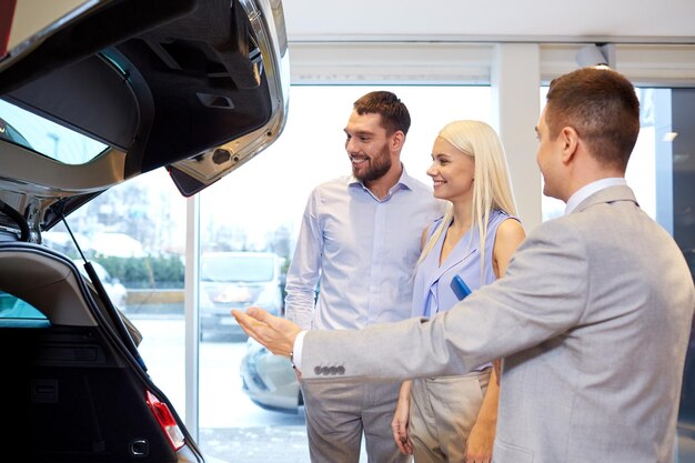 concept d'entreprise automobile, de vente de voitures, de technologie et de personnes - couple heureux avec un concessionnaire automobile dans un salon ou un salon de l'auto