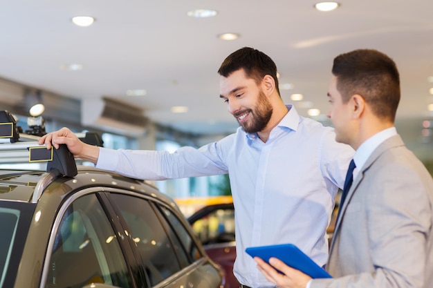 concept d'entreprise automobile, de vente de voitures, de technologie et de personnes - homme heureux et concessionnaire automobile avec ordinateur tablette dans un salon de l'auto ou un salon