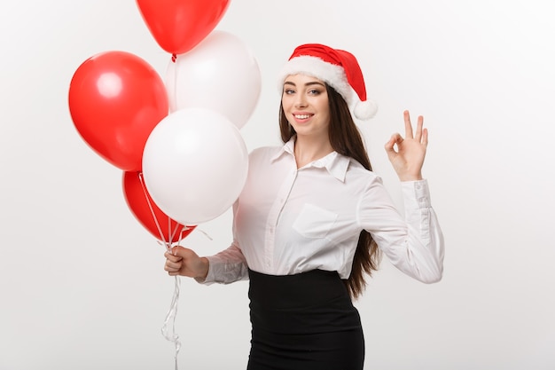 Concept d'entreprise - belle jeune femme d'affaires confiante avec bonnet de Noel tenant le ballon célébrer pour Noël.