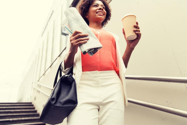 concept d'entreprise, de boissons, de style de vie et de personnes - gros plan d'une jeune femme d'affaires afro-américaine avec une tasse de café et un journal descendant au métro de la ville