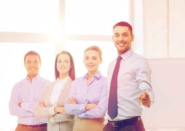 concept d'entreprise et de bureau - bel homme d'affaires souriant avec une équipe au bureau pointant du doigt vers vous