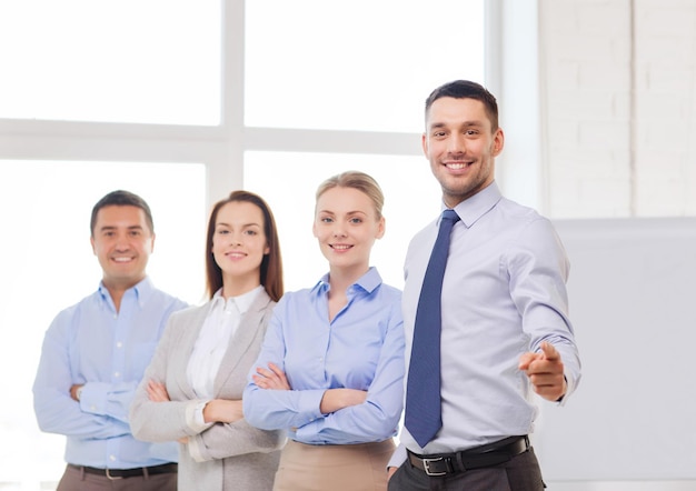 concept d'entreprise et de bureau - bel homme d'affaires souriant avec une équipe au bureau pointant du doigt vers vous