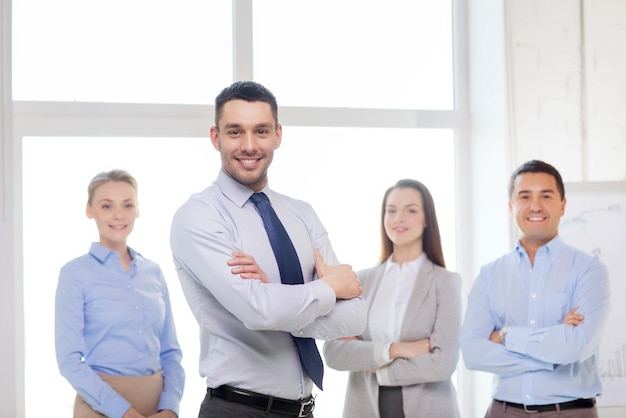 concept d'entreprise et de bureau - bel homme d'affaires souriant avec les mains croisées et l'équipe au bureau