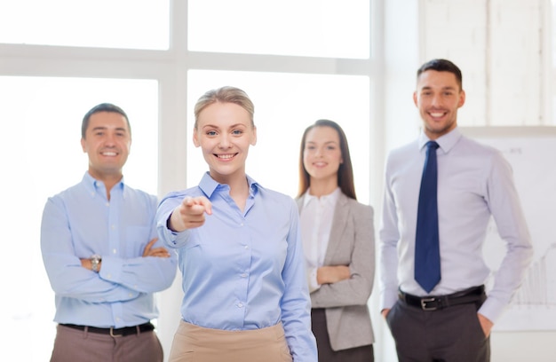 concept d'entreprise et de bureau - belle femme d'affaires souriante avec une équipe au bureau pointant du doigt vers vous