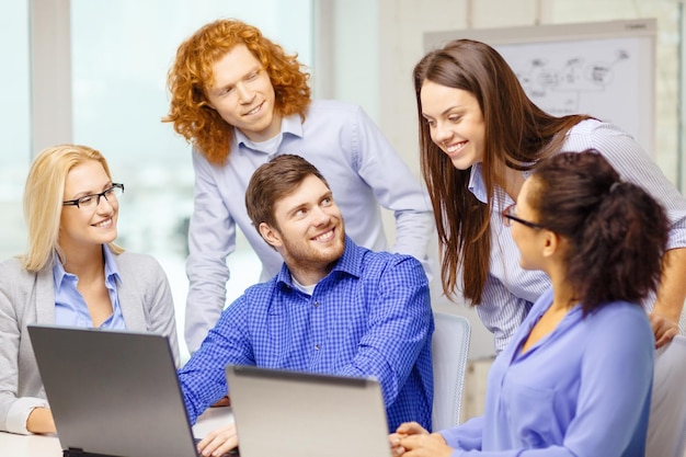 concept d'entreprise, de bureau et de démarrage - équipe créative souriante avec des ordinateurs portables travaillant au bureau