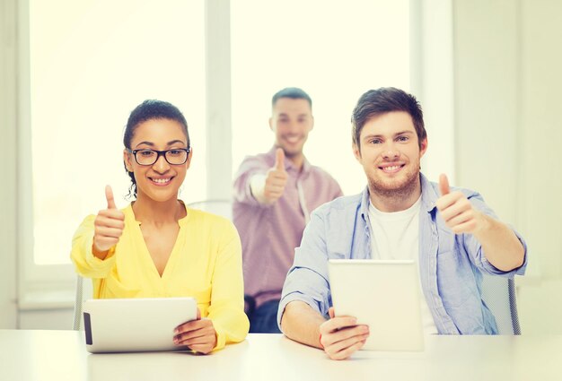 concept d'entreprise, de bureau et de démarrage - équipe souriante créative avec des ordinateurs tablettes au bureau montrant les pouces vers le haut