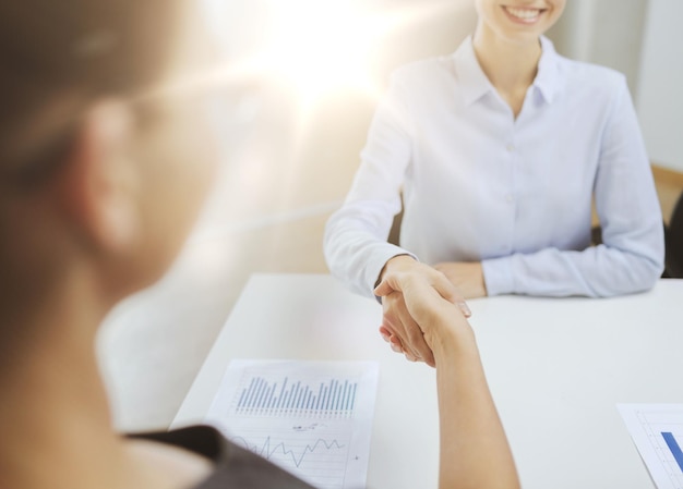 concept d'entreprise et de bureau - deux femmes d'affaires souriantes se serrant la main au bureau