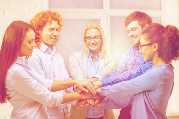 concept d'entreprise, de bureau, de geste et de démarrage - équipe créative souriante avec les mains l'une sur l'autre assise au bureau