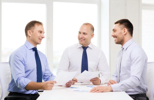 concept d'entreprise et de bureau - hommes d'affaires souriants avec des papiers au bureau