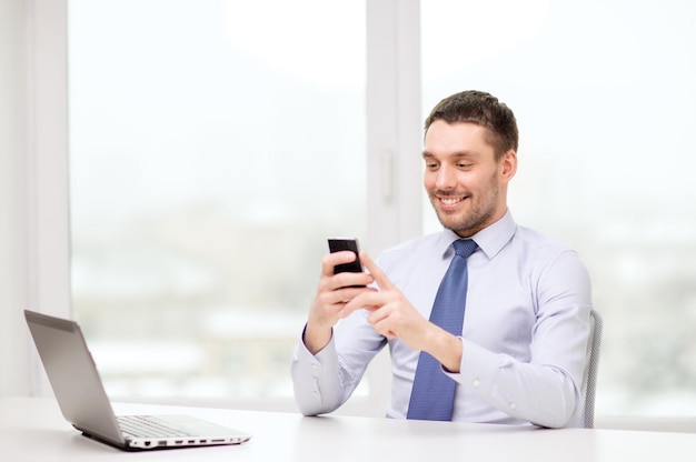 concept d'entreprise, de bureau et de technologie - homme d'affaires souriant avec ordinateur portable et smartphone au bureau