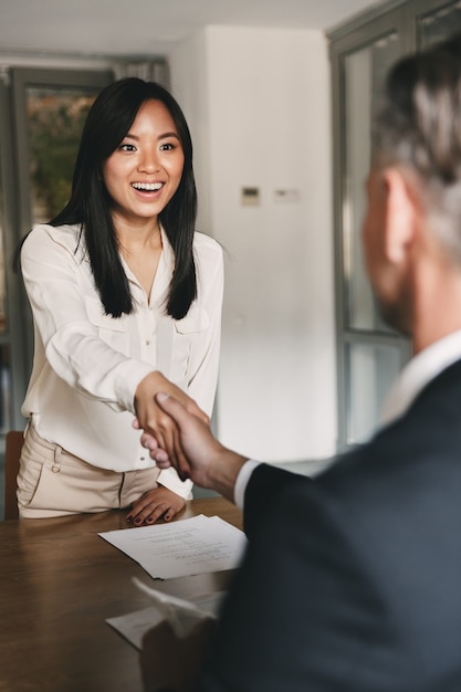 Concept d'entreprise, de carrière et de placement - heureuse femme asiatique poignée de main avec le directeur principal ou l'employeur d'une grande entreprise, après des négociations ou une entrevue réussies