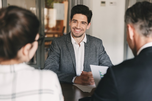 Concept d'entreprise, de carrière et de placement - jeune homme caucasien souriant, assis devant les administrateurs lors d'une réunion d'entreprise ou d'un entretien d'embauche