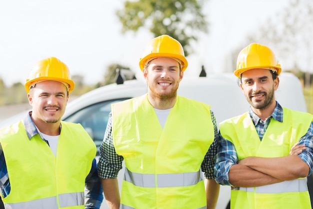 concept d'entreprise, de construction, de travail d'équipe et de personnes - groupe de constructeurs souriants dans des casques sur fond de voiture à l'extérieur