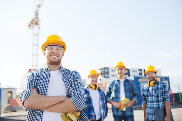 concept d'entreprise, de construction, de travail d'équipe et de personnes - groupe de constructeurs souriants dans des casques avec presse-papiers à l'extérieur