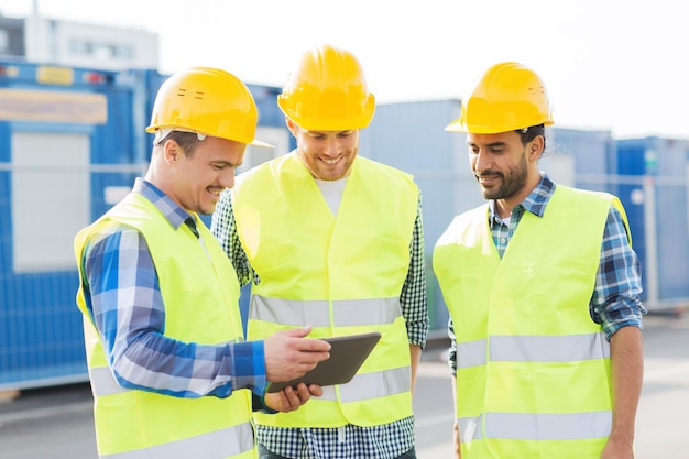 concept d'entreprise, de construction, de travail d'équipe, de technologie et de personnes - groupe de constructeurs souriants dans des casques avec tablette PC à l'extérieur