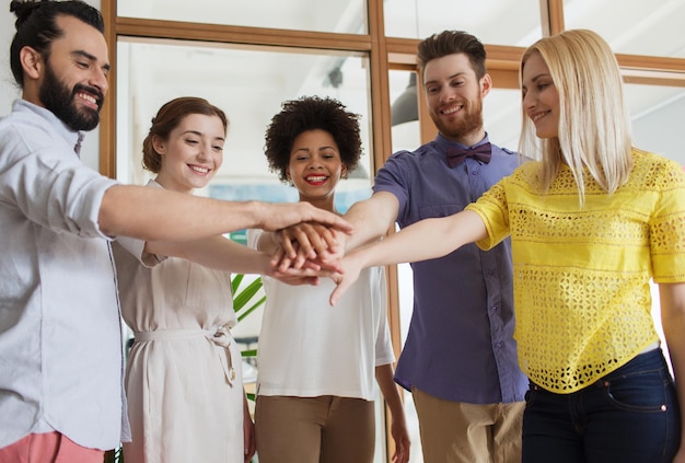 concept d'entreprise, de démarrage, de geste, de personnes et de travail d'équipe - équipe créative heureuse avec les mains les unes sur les autres au bureau