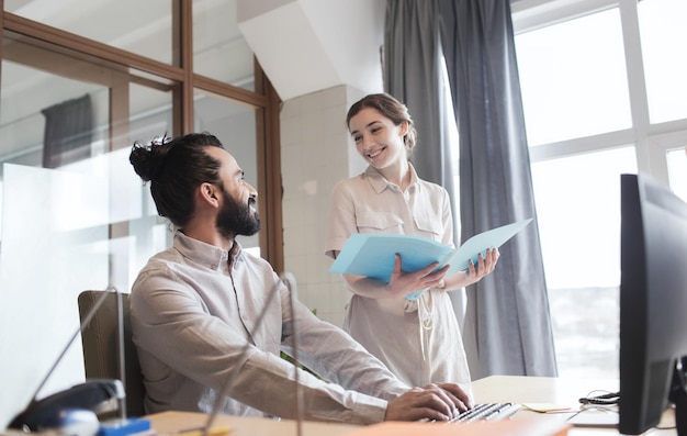 concept d'entreprise, de démarrage et de personnes - équipe créative heureuse avec ordinateur et dossier au bureau