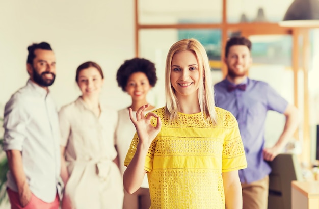 concept d'entreprise, de démarrage, de personnes, de gestes et de travail d'équipe - jeune femme heureuse montrant une main ok sur l'équipe créative au bureau