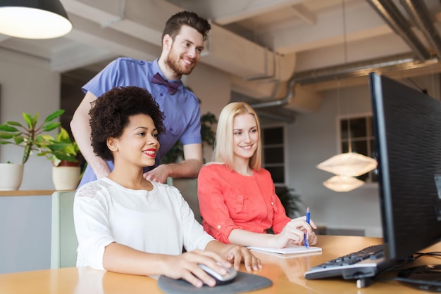 concept d'entreprise, de démarrage et de personnes - mise en réseau d'une équipe créative heureuse avec un ordinateur au bureau