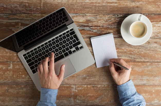 concept d'entreprise, d'éducation, de personnes et de technologie - gros plan sur des mains masculines avec un ordinateur portable et une tasse de café prenant des notes sur un carnet à l'aide d'un stylo