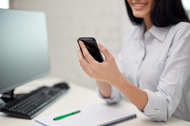 concept d'entreprise, d'éducation, de technologie et de personnes - gros plan d'une femme heureuse avec ordinateur portable et textos d'ordinateur sur smartphone au bureau