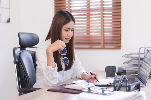 Concept d'entreprise Femme d'affaires tient des lunettes lors de la lecture et de l'écriture de données sur un document d'entreprise