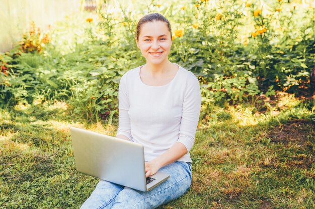 Concept d'entreprise indépendant. Jeune femme assise sur la pelouse d'herbe verte dans le parc de la ville travaillant sur ordinateur portable pc. Style de vie authentique fille étudiante candide étudiant à l'extérieur.