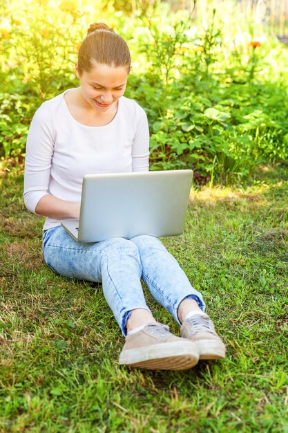 Concept d'entreprise indépendant. Jeune femme assise sur une pelouse d'herbe verte dans le parc de la ville travaillant sur un ordinateur portable. Style de vie authentique étudiante candide étudiant à l'extérieur. Bureau mobile