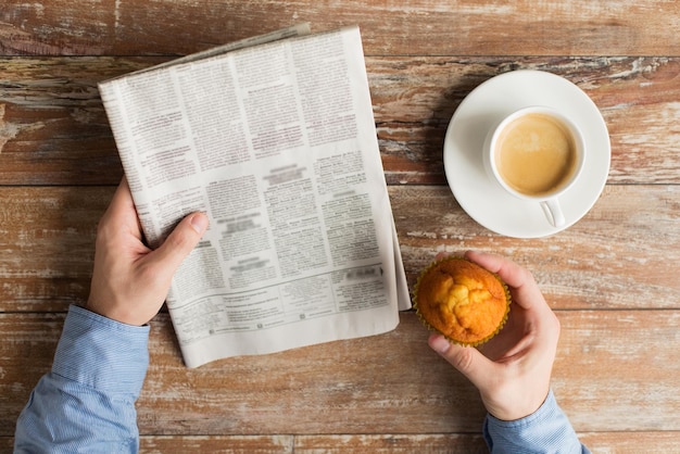 concept d'entreprise, d'information, de personnes et de médias de masse - gros plan sur des mains masculines avec du papier journal, des muffins et une tasse de café sur la table