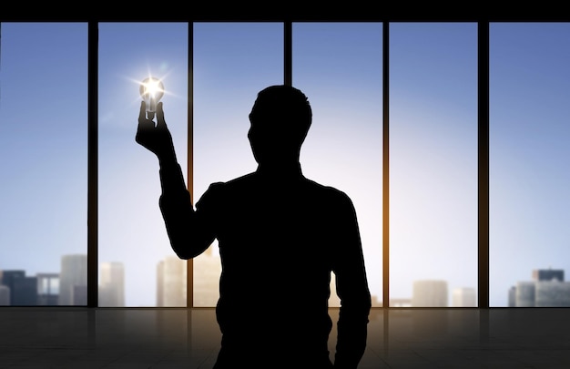 concept d'entreprise, d'inspiration, d'idée et de personnes - silhouette d'homme d'affaires tenant une ampoule allumée sur fond de fenêtre de bureau