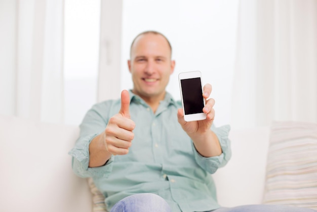 concept d'entreprise, de maison, de personnes, de gestes et de technologie - gros plan d'un homme souriant avec un smartphone à la maison