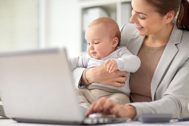 concept d'entreprise, de maternité, de multitâche, de famille et de personnes - femme d'affaires souriante heureuse avec bébé et ordinateur portable travaillant au bureau