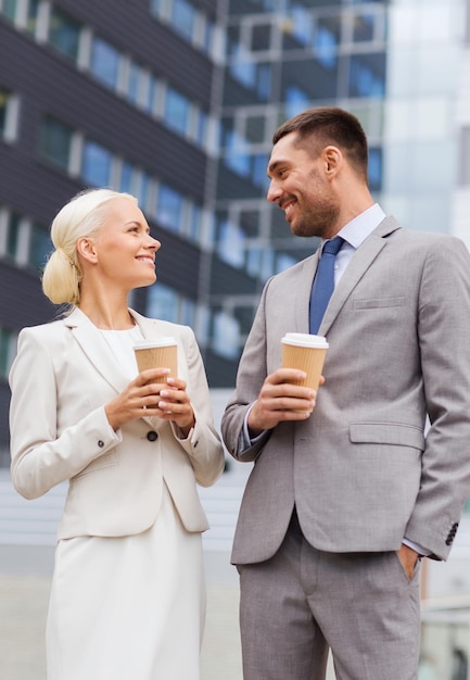 concept d'entreprise, de partenariat, de boissons chaudes et de personnes - hommes d'affaires souriants avec des gobelets en papier debout au-dessus d'un immeuble de bureaux