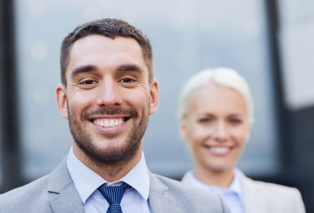 concept d'entreprise, de partenariat, de succès et de personnes - gros plan d'un homme d'affaires et d'une femme d'affaires souriants debout au-dessus d'un immeuble de bureaux