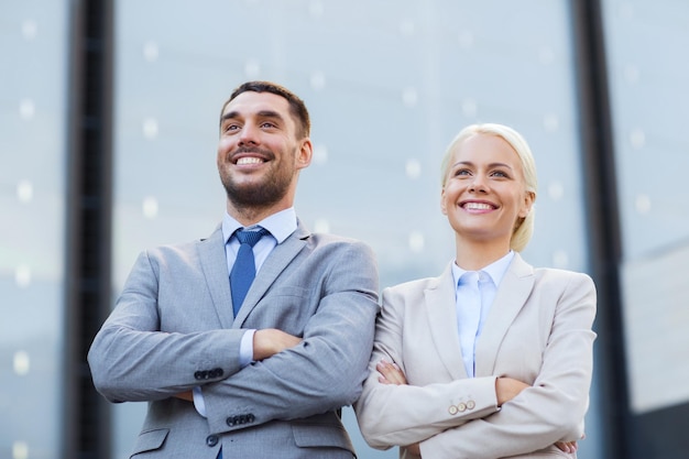 concept d'entreprise, de partenariat, de succès et de personnes - homme d'affaires et femme d'affaires souriants debout au-dessus d'un immeuble de bureaux