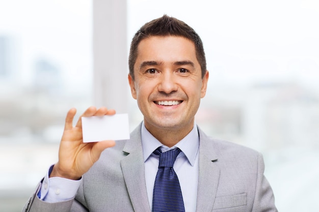 Concept d'entreprise, de personnes et de bureau - homme d'affaires souriant en costume montrant une carte de visite blanche vierge