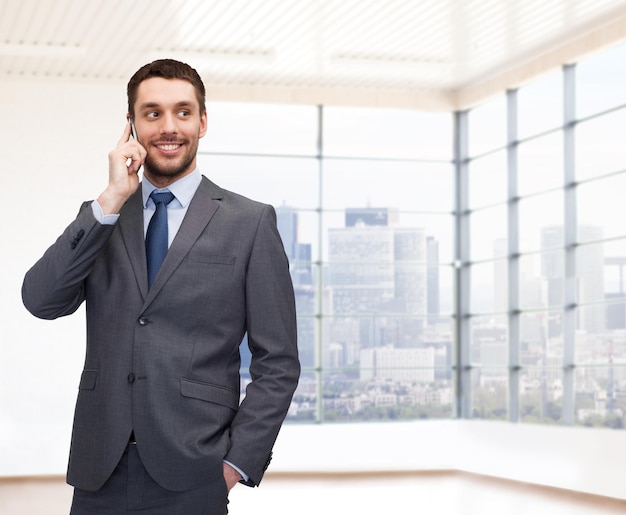 concept d'entreprise, de personnes et de bureau - jeune homme d'affaires heureux appelant sur un smartphone au-dessus d'une salle de bureau ou d'un nouvel arrière-plan d'appartement